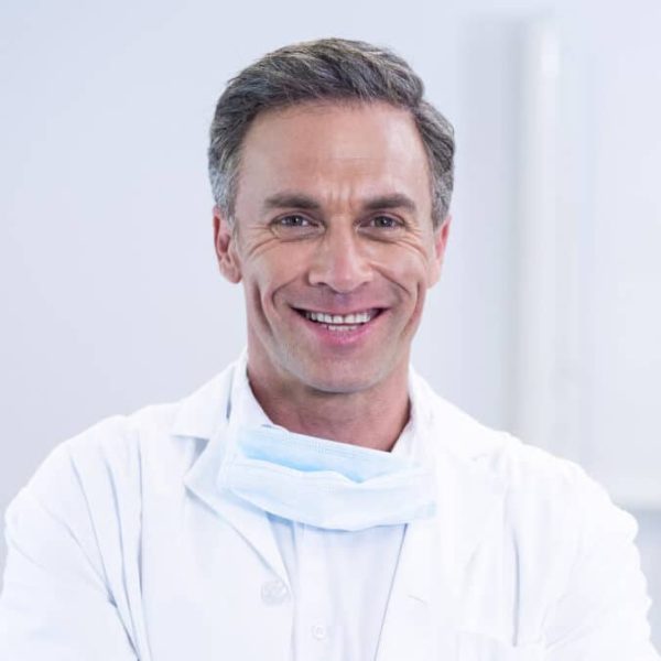 Portrait of smiling dentist standing with arms crossed in dental clinic